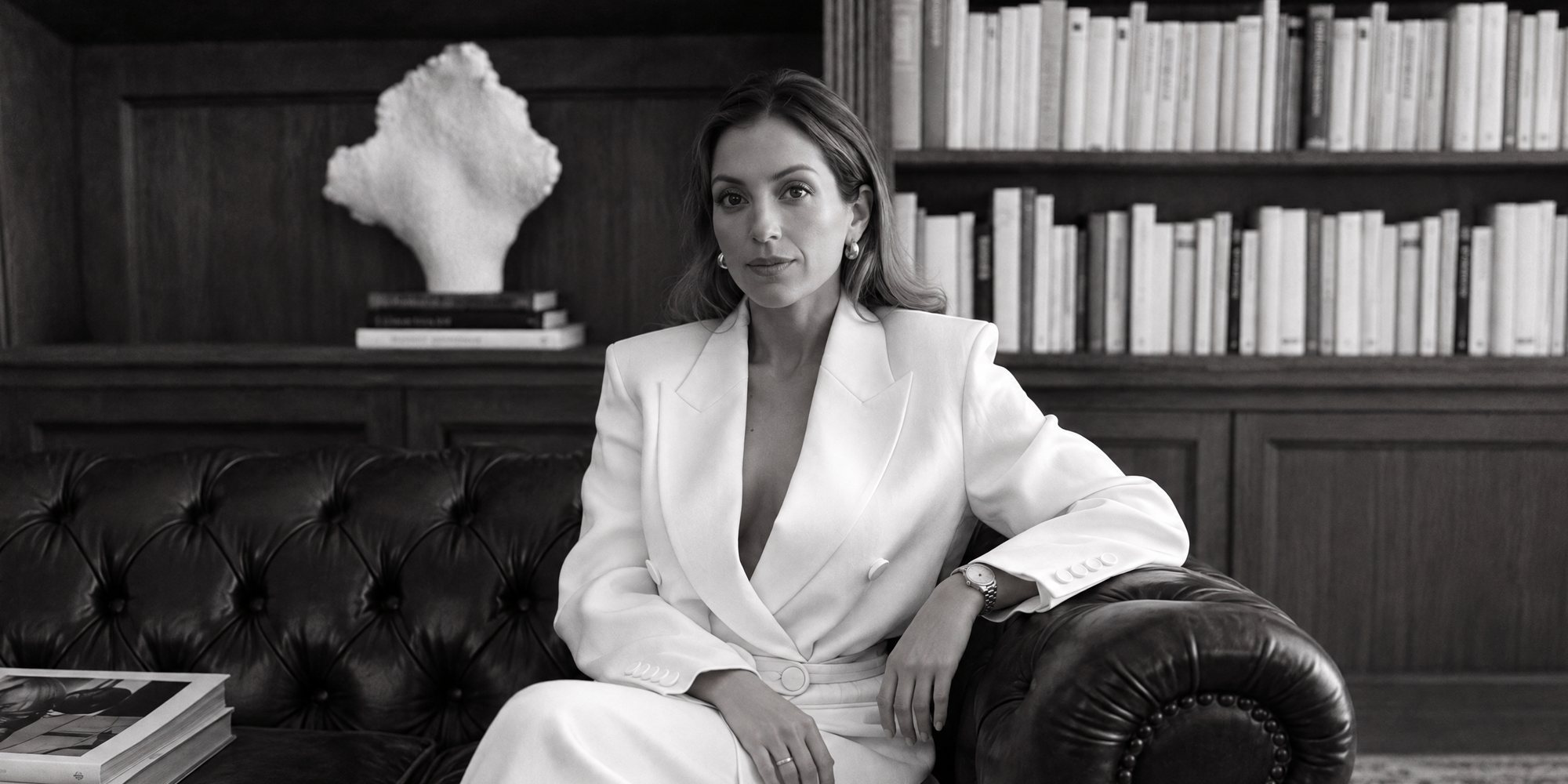 Jeanette Isabella Gunnerød in a white suit on a leather sofa in a wood-panelled library